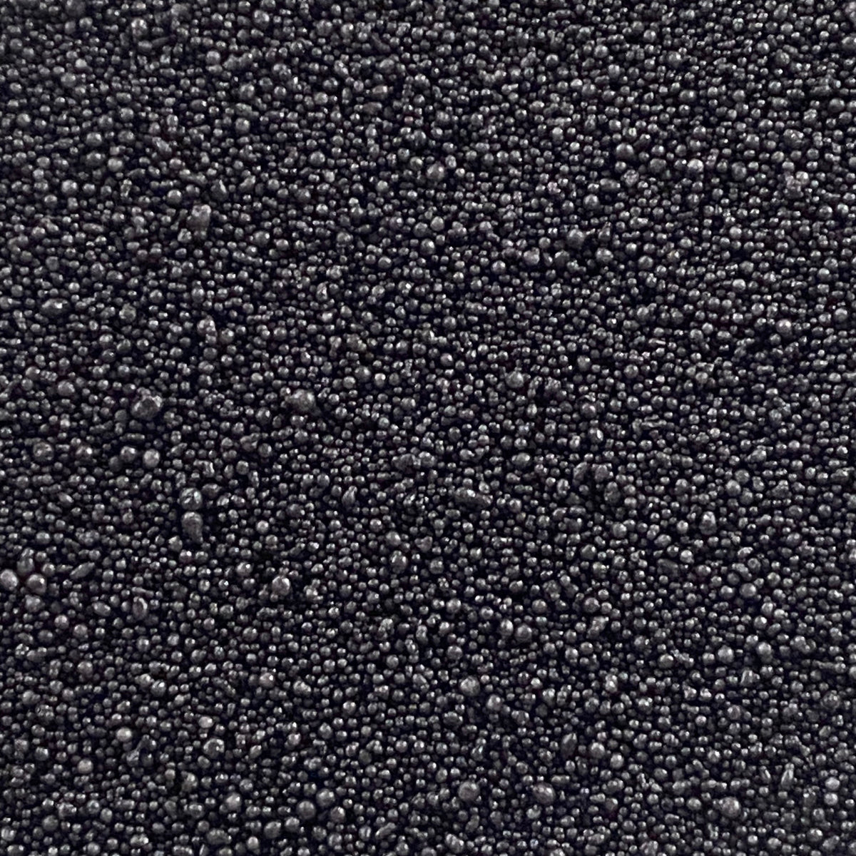 A close-up texture shot of small, dark gray to black spherical beads or granules filling the entire frame.