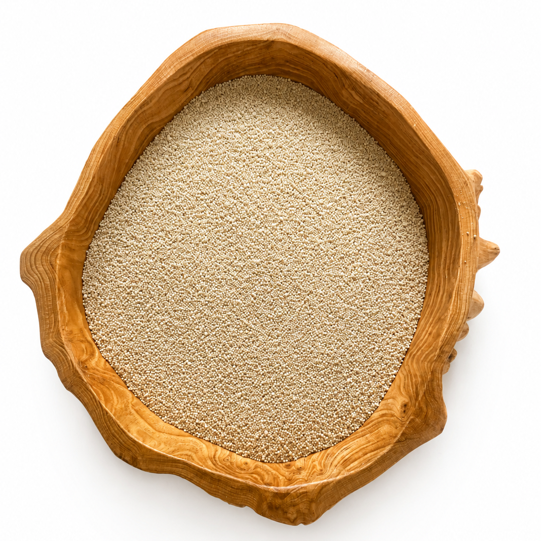 A top-down view of a light beige grain or seed mixture contained within an organic-shaped wooden bowl with a rich warm brown wood grain, set against a solid white background.
