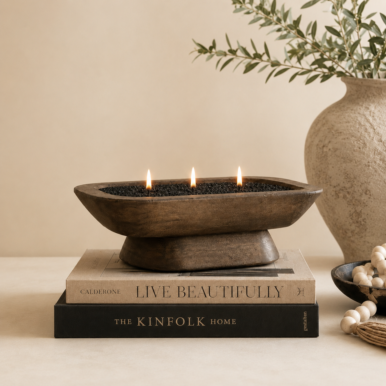 Decorative bowl with candles on books, surrounded by a vase and plants.