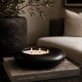 Black candle holder with three candles on a book in a cozy indoor setting