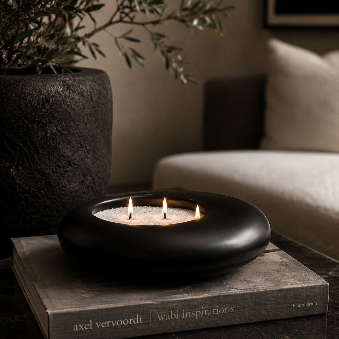 Black candle holder with three candles on a book in a cozy indoor setting