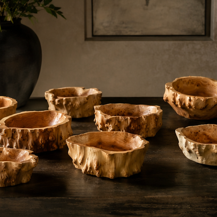 A set of rustic, hand-carved wooden bowls with textured bark-like edges, arranged on a dark wooden table in a dimly lit interior setting.