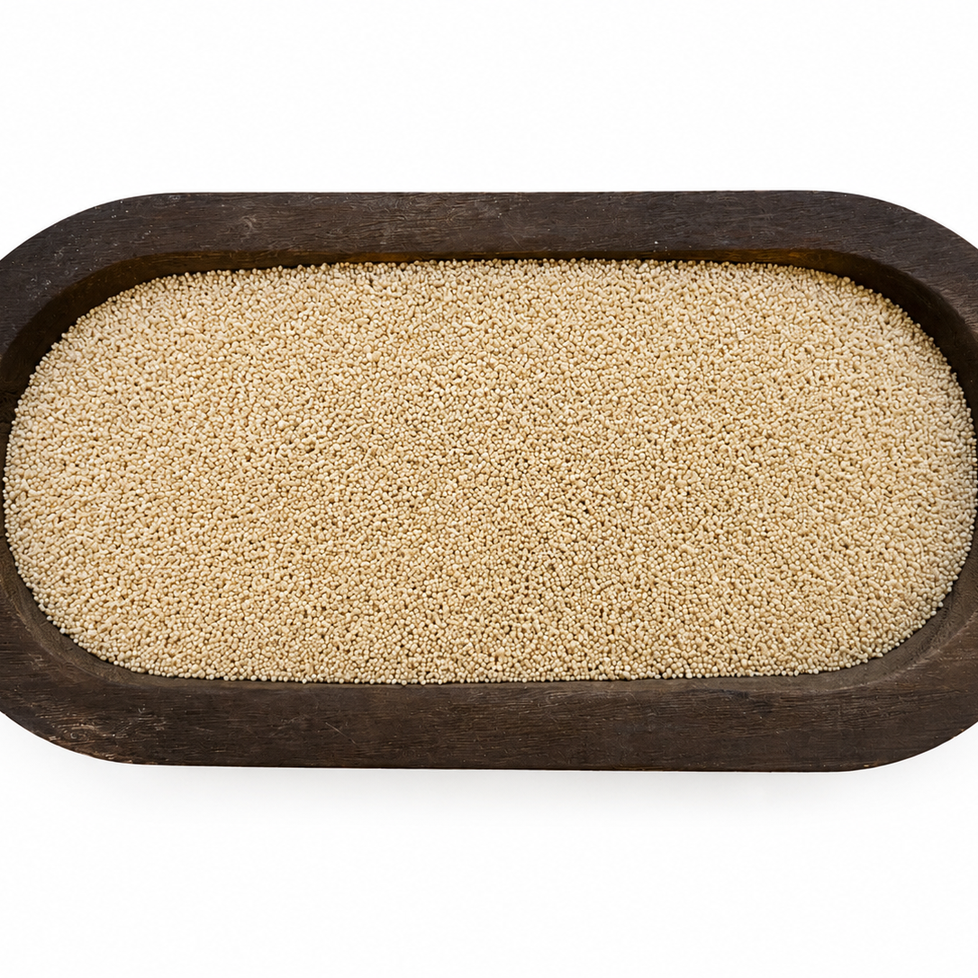 A top-down view of beige grains or seeds contained within an oval dark brown wooden tray, isolated on a white background.
