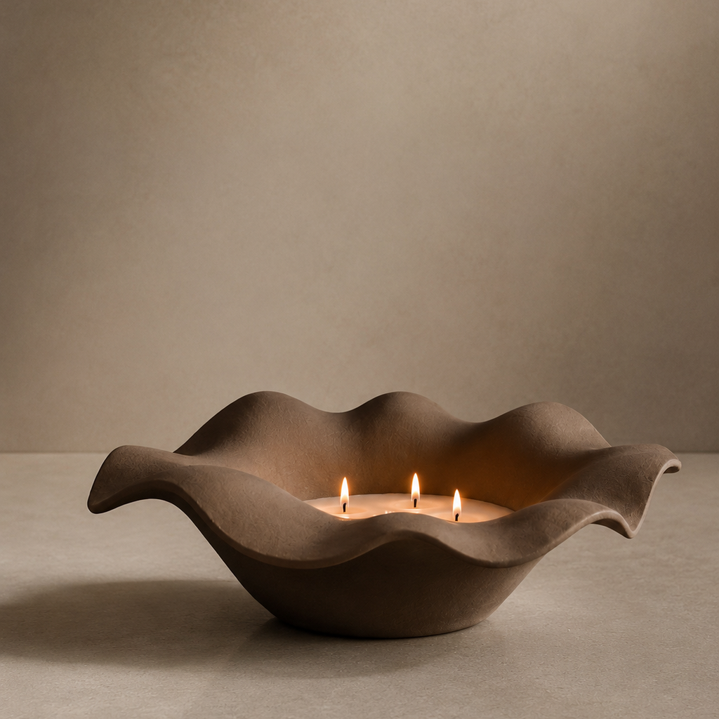 Decorative ceramic bowl with wavy design holding three lit candles on a neutral background