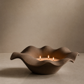 Decorative ceramic bowl with wavy design holding three lit candles on a neutral background