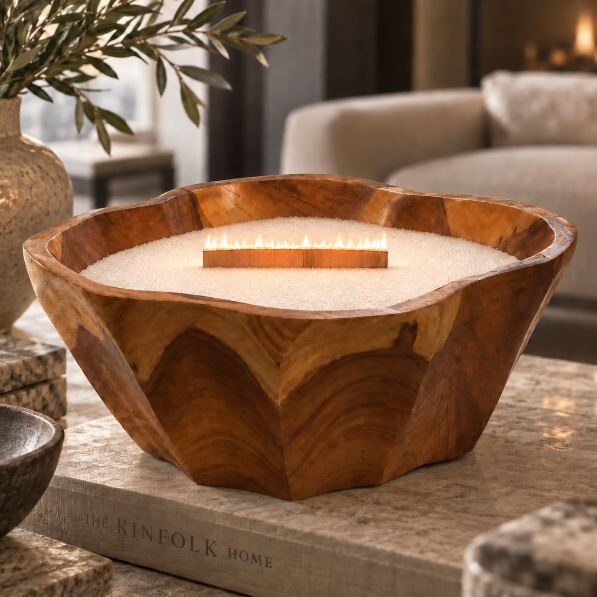 A large wooden bowl fire pit with a glowing flame, filled with white fuel pellets, styled on a stone table in a cozy living room setting.