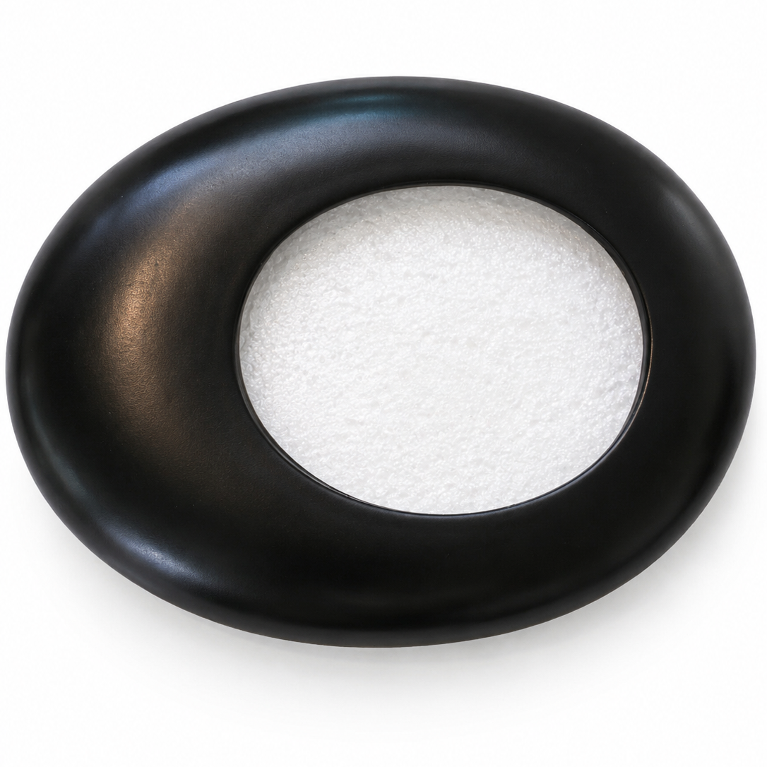 A black oval-shaped tray or dish with a circular cutout in the center revealing a white textured insert, shown on a plain white background.