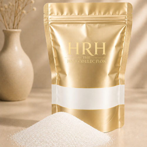 A metallic gold stand-up pouch labeled 'HRH THE HRH COLLECTION' with a white horizontal band, standing on a beige surface with a small pile of white powder in front. A beige vase with dried stems sits blurred in the background.