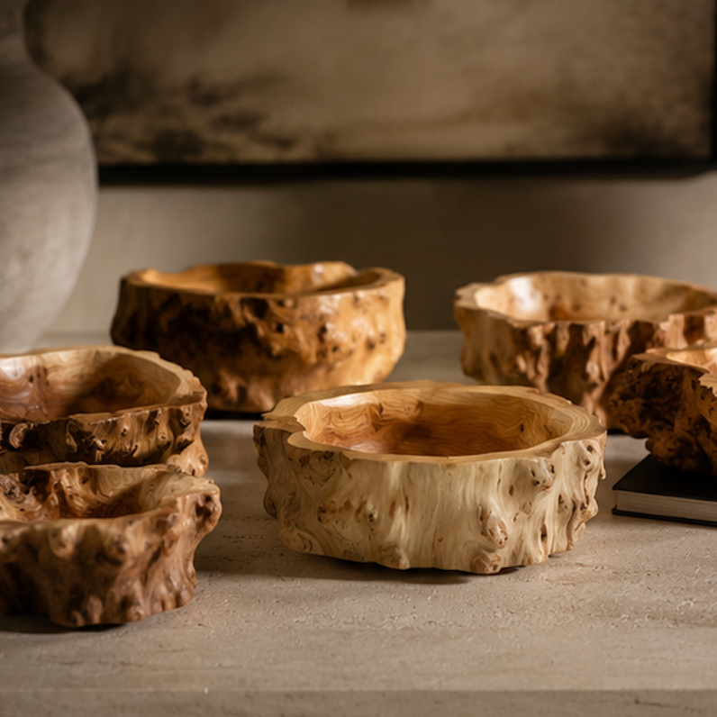 Six rustic hand-carved wooden bowls with natural bark-like edges, arranged on a stone surface in a styled interior setting.